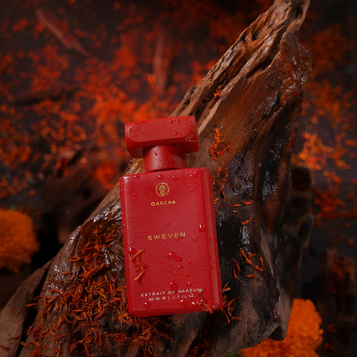 Front view of Sweven 50 milliliter extrait de parfum bottle showcasing its red finish and water droplets on dark driftwood with orange flowers